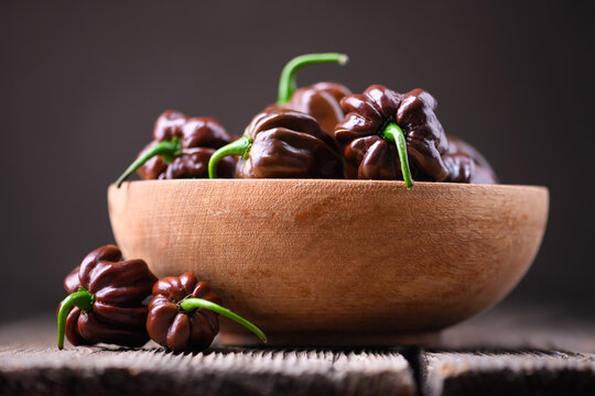 Chocolate habanero peppers in wooden bowl close view. Fresh chili pods natural texture shallow depth composition