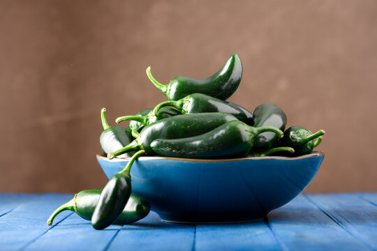 Bowl filled with jalapeno peppers on blue wooden table with warm blurred background. Fresh chili, organic vegetables, rustic contrast, food concept
