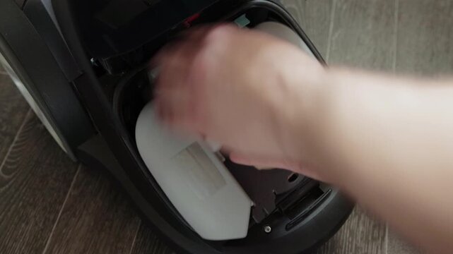 Close up view of person hands inserting new dust bag into empty bag compartment of modern vacuum cleaner, showing steps for home appliance upkeep and clean living space.