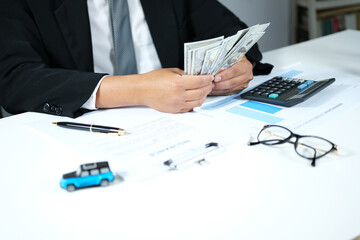 Fototapeta premium A businessman counts money at his desk for car insurance, vehicle maintenance, vehicle purchases, and rentals. Business and transportation concepts 