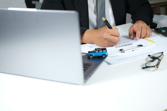 Car purchase and insurance agreement. Signing a car dealership contract. Automotive purchase agreement. Car insurance coverage. Monthly debt burden. Vehicle collateral on a desk in front of a laptop.