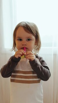 Vertical video. Little child blowing party horn during birthday celebration at home. Close-up candid moment of playful kid enjoying family party indoors in daylight. Slow motion 4K footage.