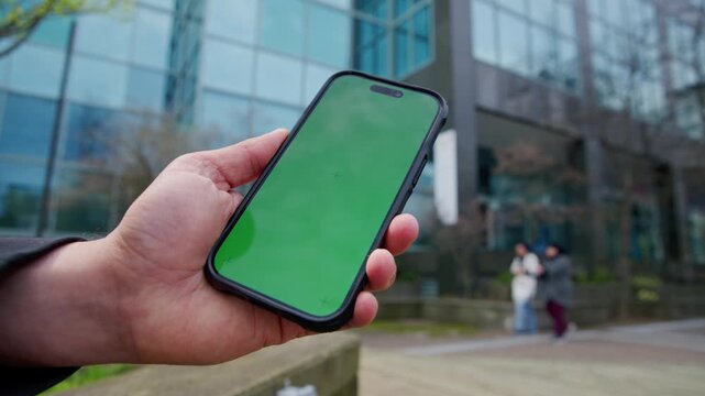 A man pauses on the street, holding a smartphone with a bright screen. He interacts with the device, surrounded by the buzz of urban life