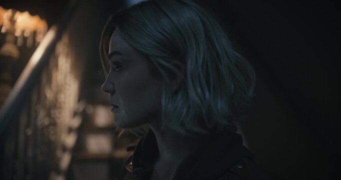 Handheld, closeup shot of blonde woman with flashlight being startled by camera in haunted house