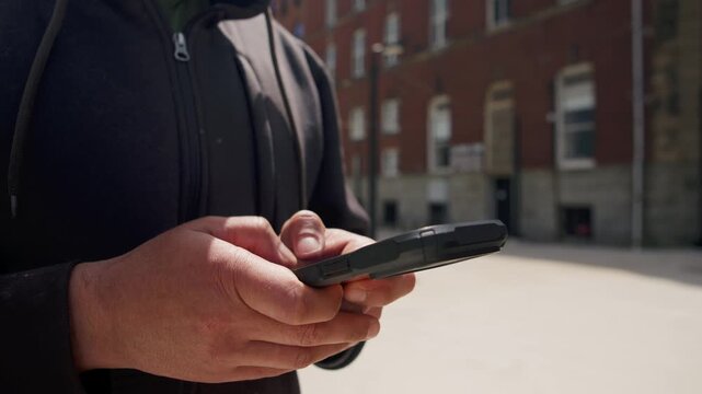 A man stands on a bustling street, focused on his smartphone. His hand skillfully navigates the screen, showcasing the wonders of modern technology