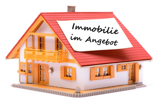 Ein Zettel klebt auf dem Dach von einem Modellhaus mit der Aufschrift: Immobilie im Angebot