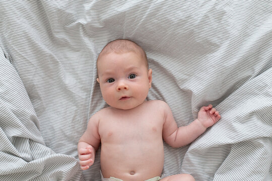 A cute little 3-month-old baby boy is lying on a bed with a white striped sheet. Newborn.