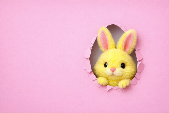 A cute yellow plush bunny peeks out from a hole cut in cardboard with a pink background, creating an adorable Easter decoration or gift box design.