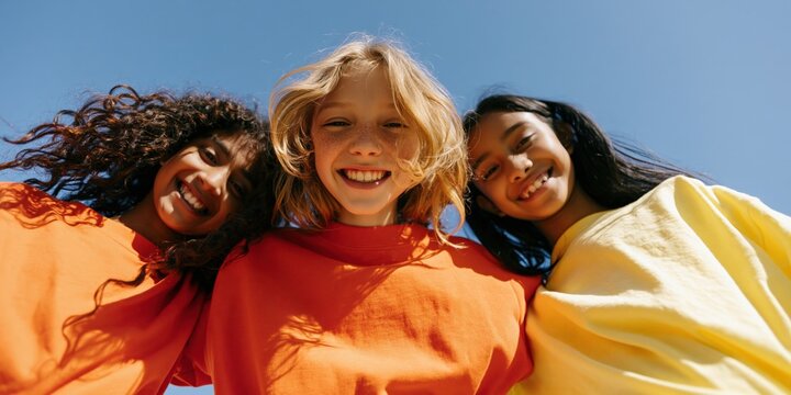 Smiling trio of children in colorful shirts under blue sky for friendship banner background and youth campaign design