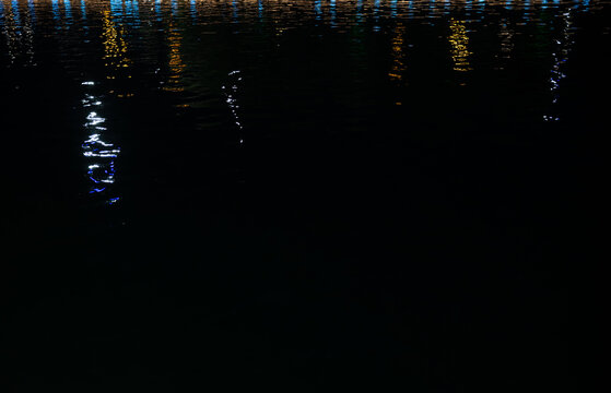 Colorful light reflections on water ripples at night, abstract neon background with copy space.