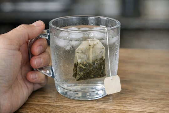 A person holds a tea bag in a glass of water, ready to steep
