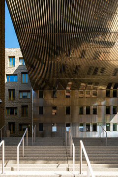 Covered entrance in La Confluence, Lyon, France leads beneath a wooden canopy, where stairs and courtyard architecture frame a quiet facade