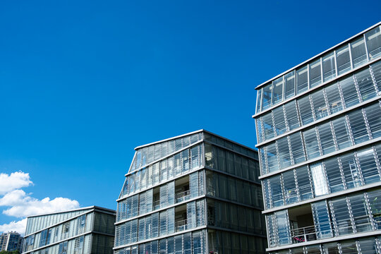 Glass buildings in La Confluence, Lyon, France step across blue sky, where architecture facade grids catch daylight above a modern urban district
