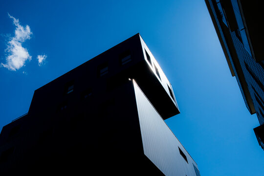 Angular building silhouette in La Confluence, Lyon, France rises from deep shadow, turning a facade into sharp architecture against clear sky