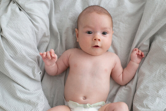 A cute little 3-month-old baby boy is lying on a bed with a white striped sheet. Newborn.