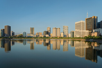 Naklejka premium Golden sunlight illuminates modern office towers and residential skyline reflected across Cau Giay Lake in Hanoi, Vietnam.