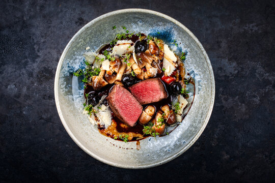 Roasted venison steak from haunch with wild mushrooms volvaria volvacea, black cherry fruity sauce with red wine and parmesan served as top view in a design bowl