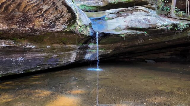 View of a small waterfall flowing over layered sandstone rocks into a pool at Hocking Hills State Park, Logan, Ohio, United States.