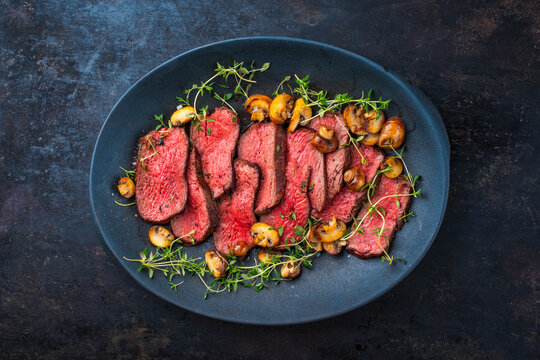 English medium broiled tagliata di manzo beef steak meat with roasted mushrooms and fresh herbs served as top view on a design plate