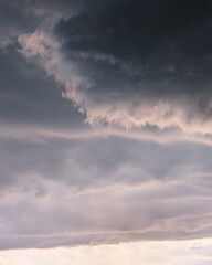 Obraz premium Moody storm clouds at sunset with soft pink light. Heavy, dark storm clouds rolling over a pale pink and grey sunset sky. Atmospheric, textured cloudscape before a summer rainstorm.