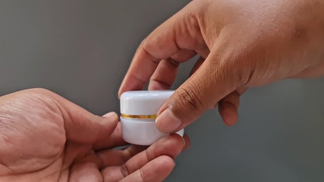 Sidoarjo, Indonesia - 24 May, 2026: Hand Holding Open White Face Cream Jar on Gray Background, Blank Skincare Product Mockup for Beauty Branding