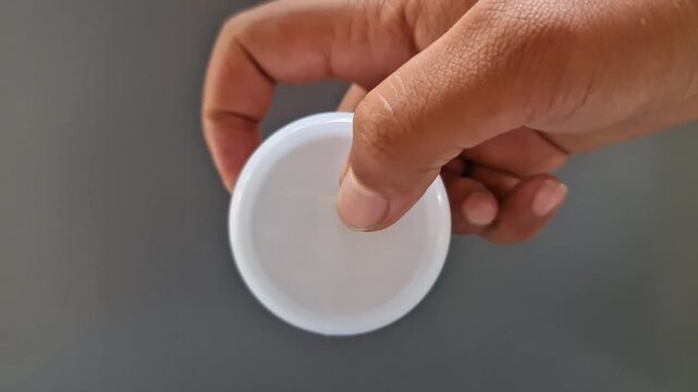 Sidoarjo, Indonesia - 24 May, 2026: Minimalist Open White Skincare Cream Jar Held in Hand on Solid Gray, Clean Beauty Product Mockup with Copy Space