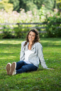 Young happy woman sitting in grass and using an ipad. 