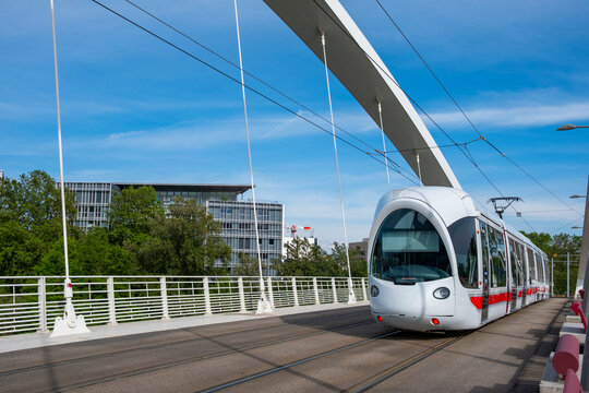 Modern tram crosses a bridge in Lyon, France beneath overhead wires, linking urban transport with tracks, architecture, and blue sky