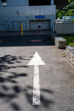 White arrow marking on asphalt road leads toward an urban building entrance, where driveway shadow and geometry shape a quiet service approach