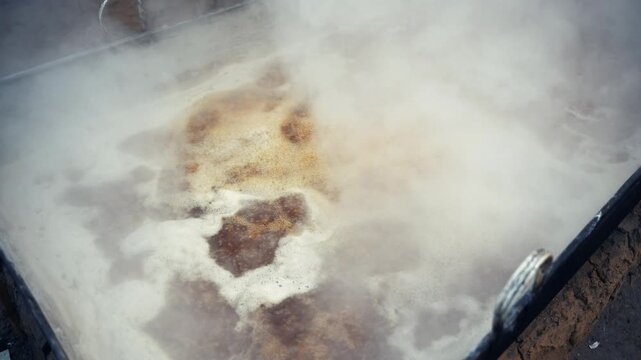 View of boiling jaggery liquid with thick steam rising from a large metal vat during traditional production in Natore, Rajshahi Division, Bangladesh.