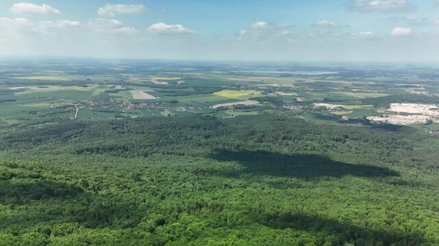 Aerial view of vast forest and farmland plain with a quarry stretching to the horizon under a blue sky in summer