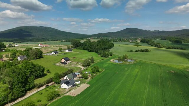 Aerial view of a rural village with houses fields and a pond below forested hills in summer