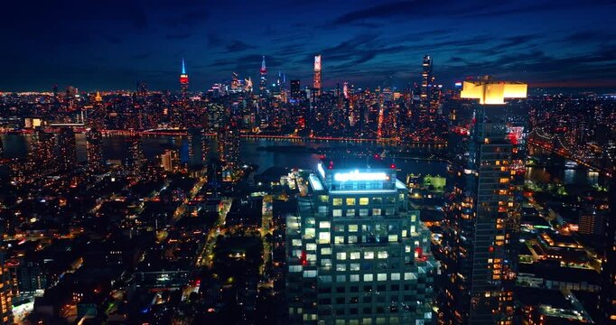 Flight at the tops of high-rises with neon illumination on top. Night panorama of New York City, USA with gorgeous city lights.