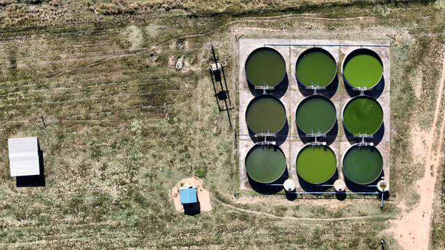 Aerial view of nine circular green water tanks arranged in a grid on a concrete pad surrounded by dry grassy fields South Africa.