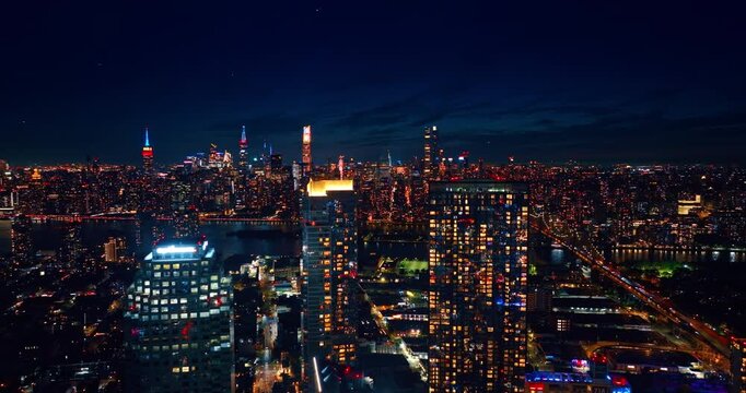 Approaching the neon tops of the high-rises with glossy facades. Drone flight over stunning New York City at night.