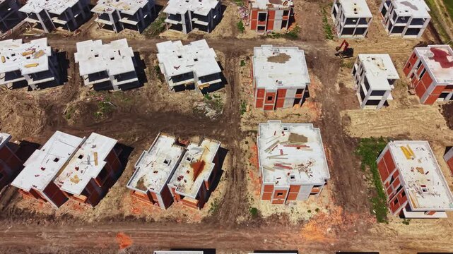 Construction workers are visible at a site with multiple unfinished buildings. The ground shows signs of excavation and development activity.