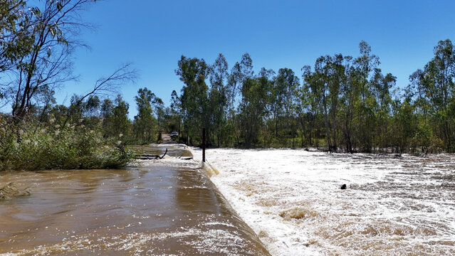 Aerial view of the Limpopo river crossing with brown rushing water over a low-level bridge surrounded by dense green trees under a clear blue sky Limpopo, Limpopo, South Africa.