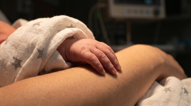 Close up of tiny baby fingers resting on mother in clinic