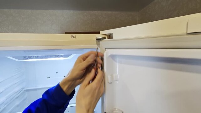Hand of a person in blue shirt adjusting the top hinge of a refrigerator door, showing a step-by-step process of maintenance in a well-lit kitchen environment