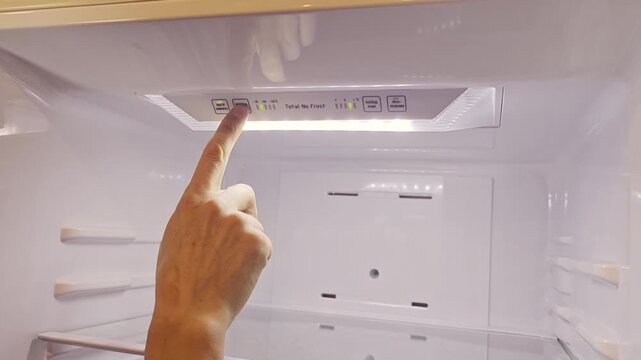 Hand pressing control button on refrigerator interior panel to adjust temperature settings, showcasing clear digital display and organized storage space