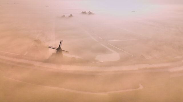 Aerial view of the historic De Vier Winden drainage mill emerging from thick morning mist over the Lage Hoek polder landscape Opmeer, North Holland, Netherlands.