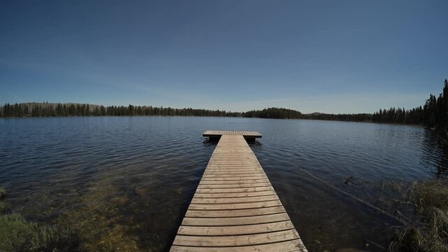 Wide angle view along a wooden dock on a small northern lake with small waves on the water and a blue sky
