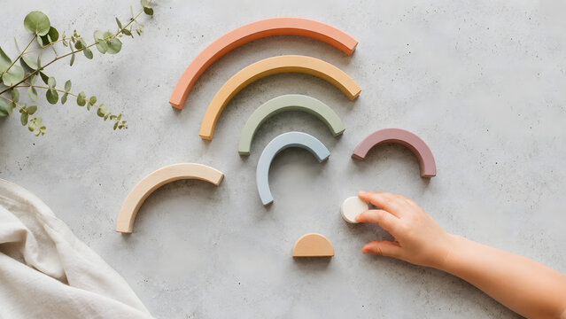 Close up of toddler hand playing with wooden rainbow stacker toy on concrete table
