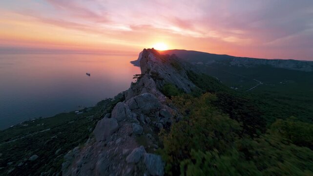 Flying over a mountain range against the background of the setting sun. The sea is visible below. High quality 4k footage FPV drone shoot