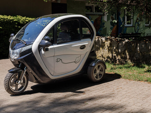 Compact electric microcar parked outdoors near residential area on sunny day. Concept of sustainable urban mobility, eco transport and modern city transportation.