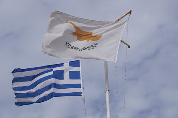 Fototapeta premium Close up of the Cyprus flag and the Greek flag waving in the wind in front of a cloudy sky, with the two flags symbolizing political and cultural unity