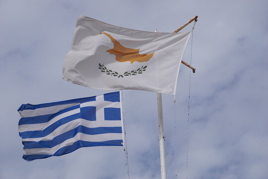 Close up of the Cyprus flag and the Greek flag waving in the wind in front of a cloudy sky, with the two flags symbolizing political and cultural unity