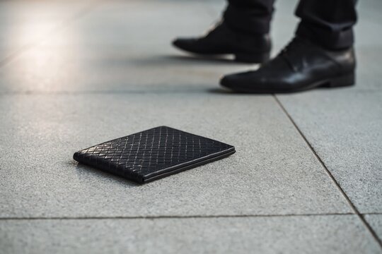 Person walking past lost black wallet on ground