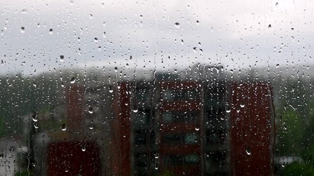 Rain falls on windows of buildings in urban area on cloudy day