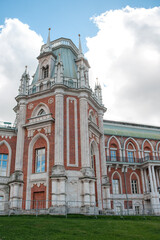 Naklejka premium The grand palace of Tsaritsyno stands tall with intricate architecture and detailed brickwork, surrounded by lush green grass and a picturesque sky.
